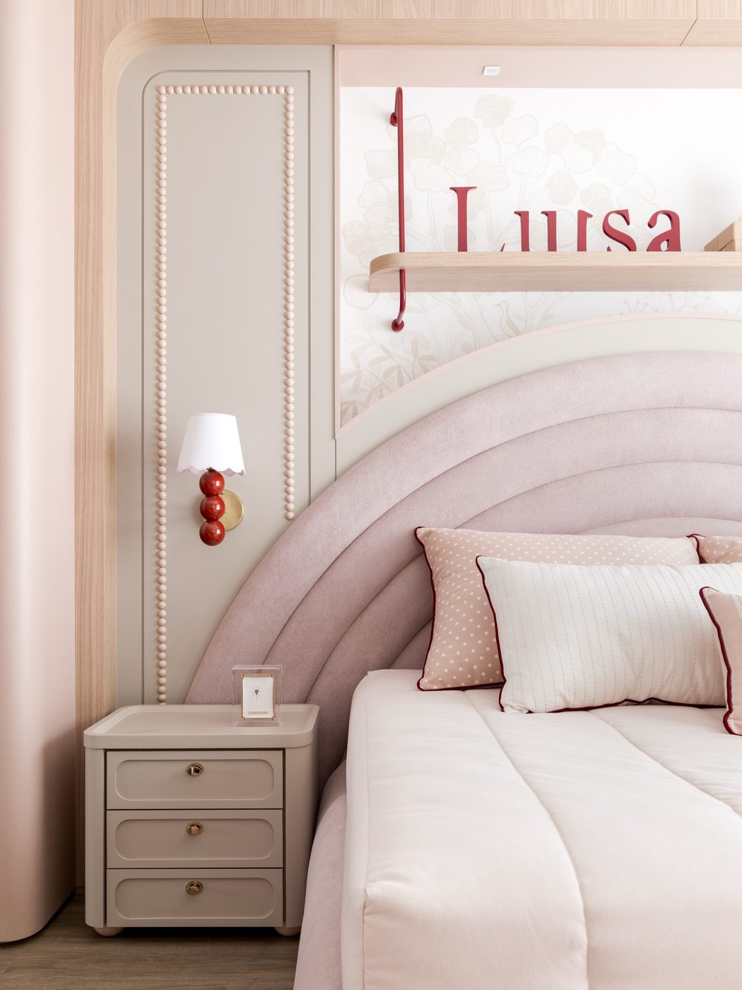 Quarto infantil rosa com cabeceira em arco, arandela vermelha e nome Luísa na parede